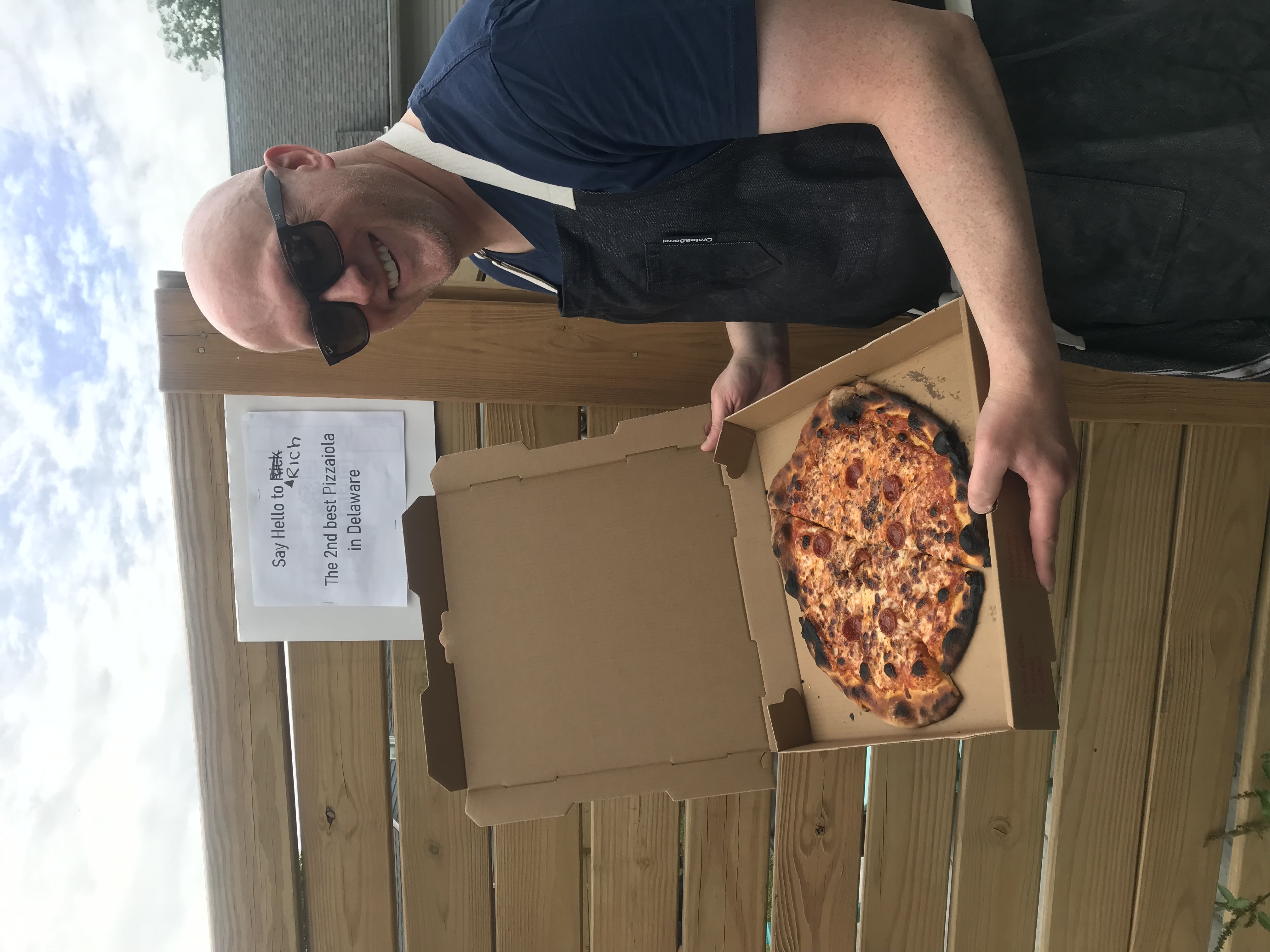 A man holding up a great pizza in a box smiling for the camera.